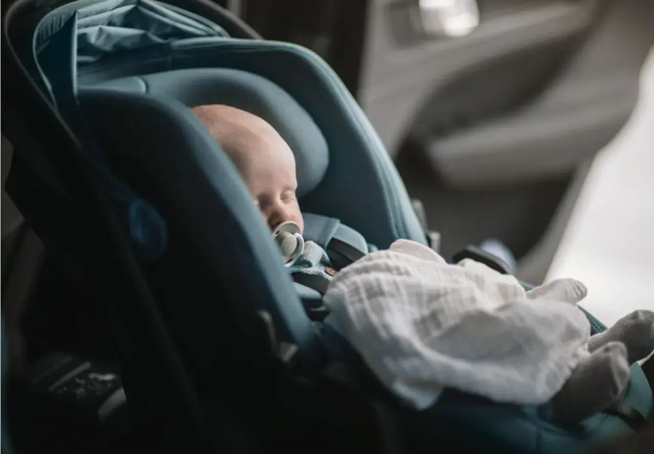 Sovande bebis med napp i en Thule babysitter, tryggt och bekvämt för resan.