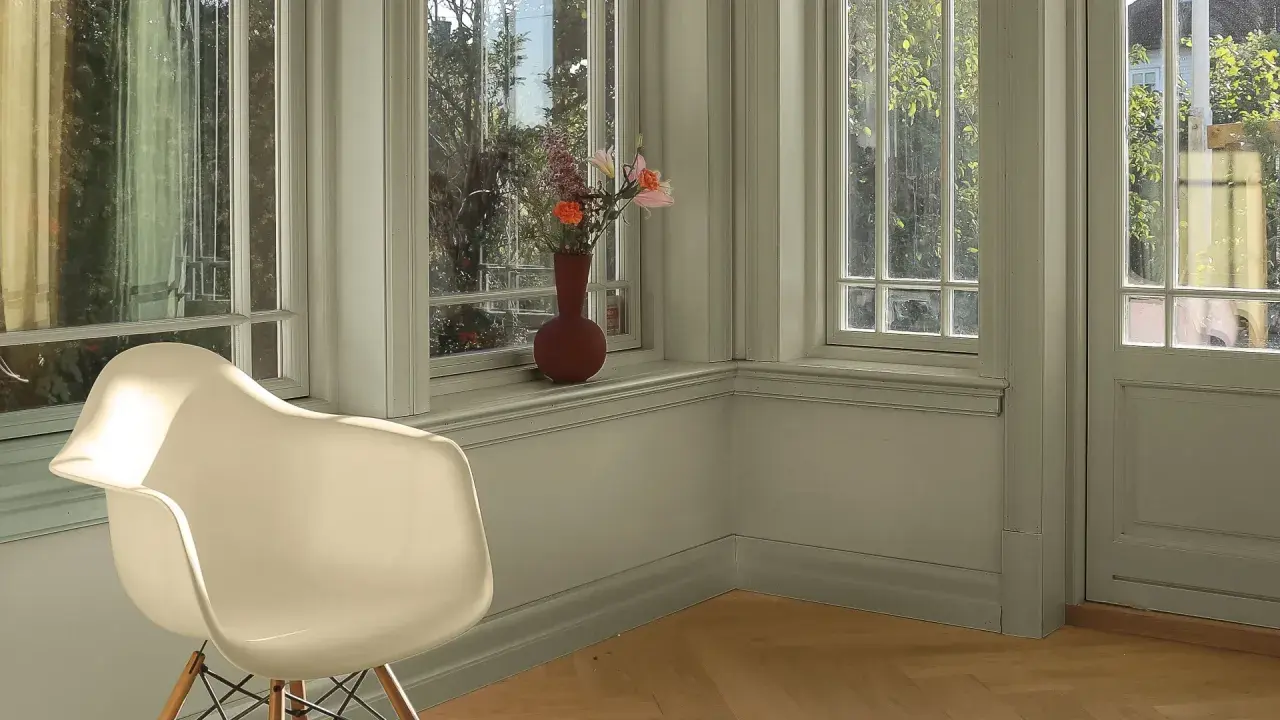 En ljus hall med en vit stol och en vas med blommor på fönsterbrädan. Perfekt måla hall inspiration för en lugn och inbjudande atmosfär.