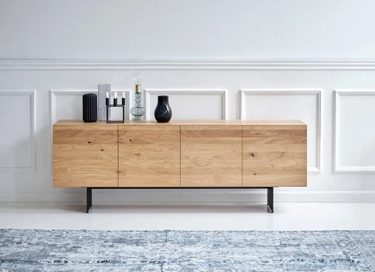 Ett stilrent sideboard i ljust trä med svarta ben, dekorerat med vaser och en lampa.
