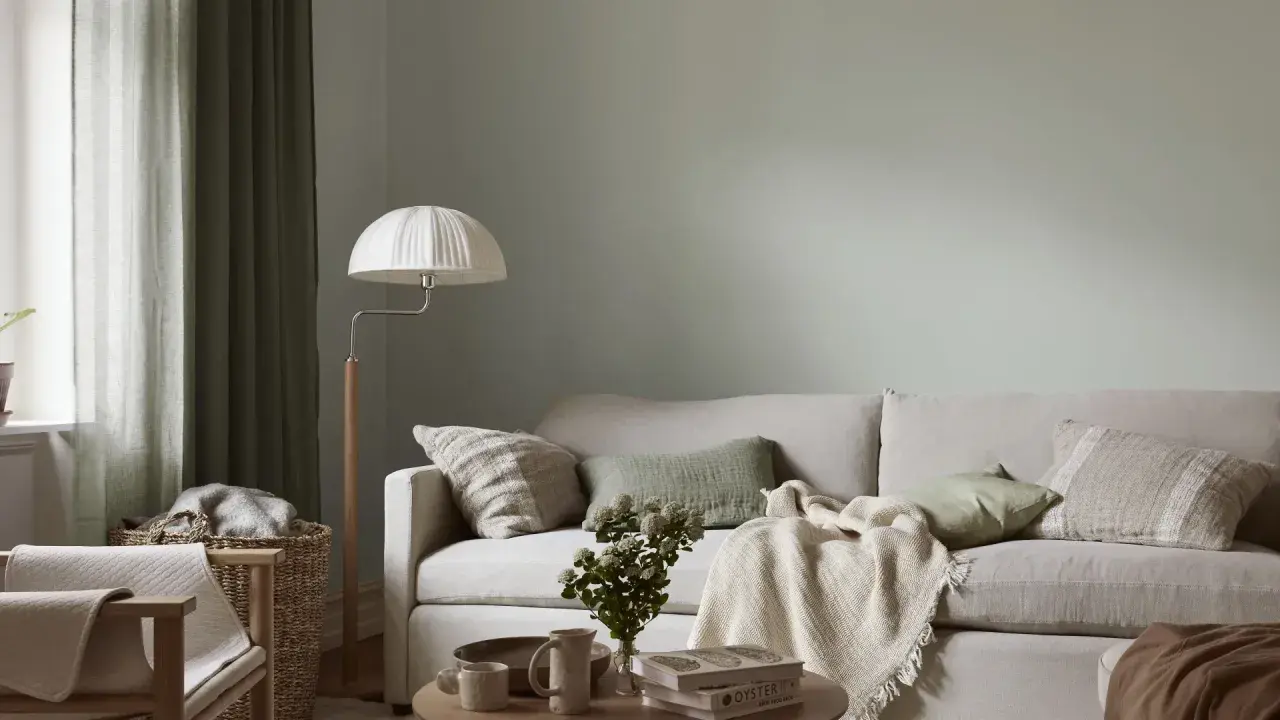 Lugnt och harmoniskt vardagsrum med ljus soffa, gröna kuddar och en vit golvlampa. Perfekt måla vardagsrum inspiration för en avslappnad atmosfär.