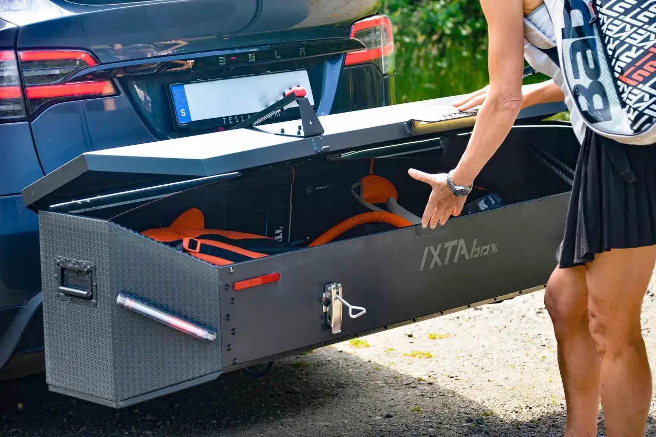 En person packar ner utrustning i en robust låda, en av många praktiska Thule produkter, fäst på en Tesla.