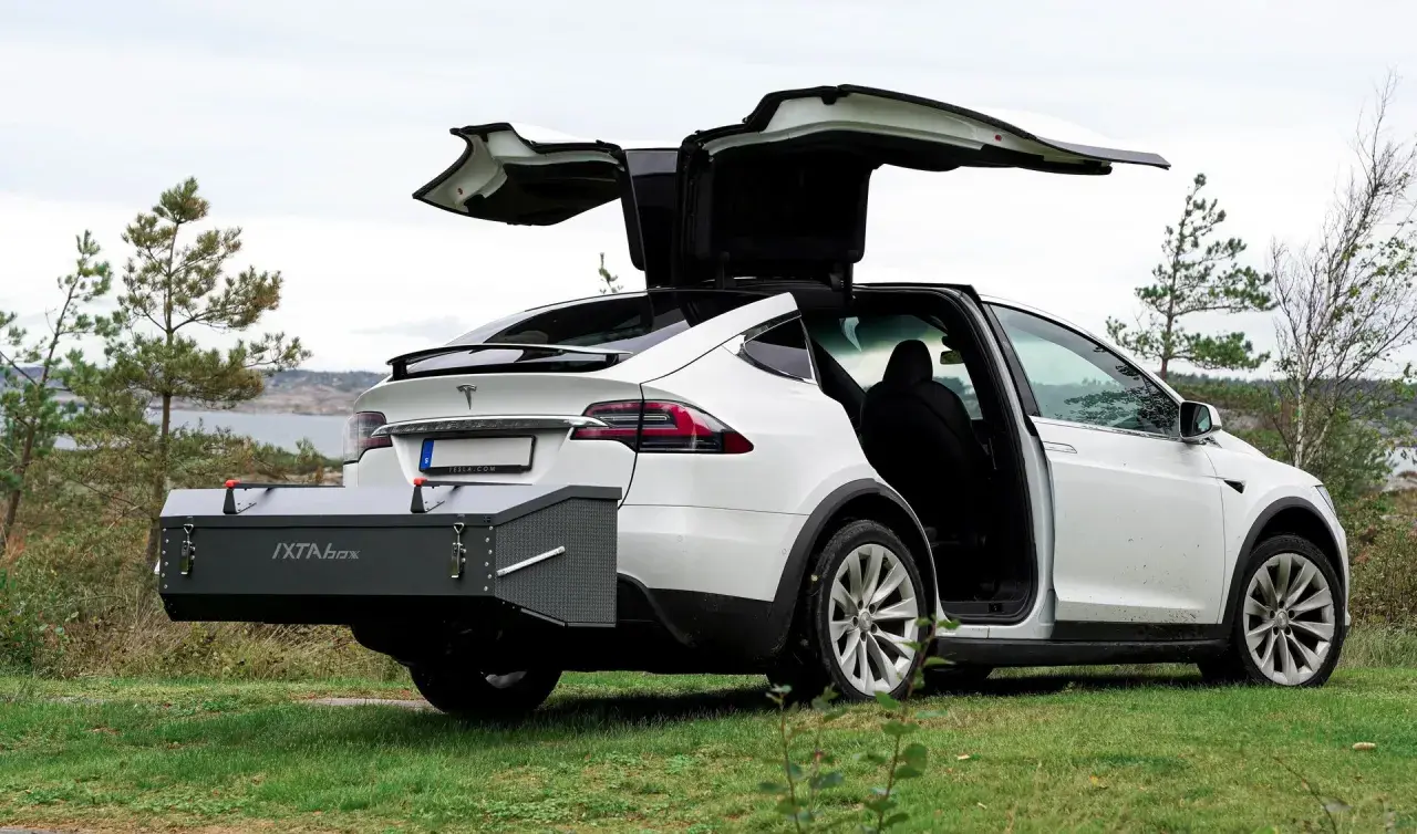 Vit Tesla Model X med bakluckan och dörrarna öppna. En smal takbox, IXTA box, är monterad baktill.