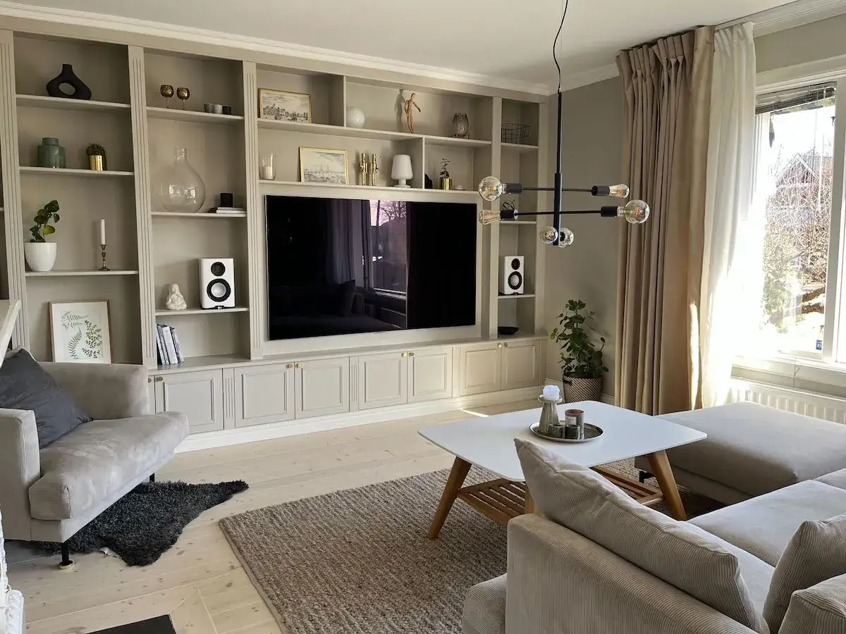 Vardagsrum med en stor, ljusgr&aring; bokhylla som rymmer TV, h&ouml;gtalare och dekorationer. En mysig soffgrupp och ett vitt soffbord skapar en inbjudande atmosf&auml;r. Ett perfekt exempel p&aring; ett lyckat bostad DIY-projekt.