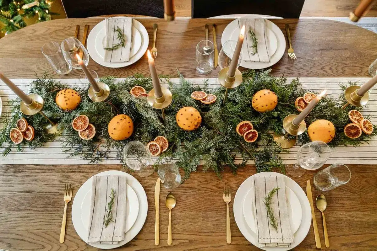 Ett vackert dukat bord med granris, apelsiner med nejlikor, torkade apelsinskivor och ljus skapar ett mysigt litet julbord.