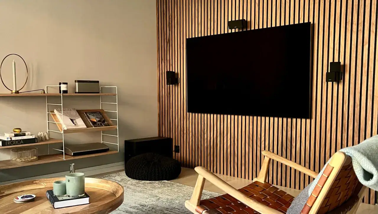 Snyggt s&auml;tt att bygga in tv i en v&auml;gg med tr&auml;lameller. En bekv&auml;m f&aring;t&ouml;lj och hyllor med b&ouml;cker och dekorationer skapar en mysig atmosf&auml;r.
