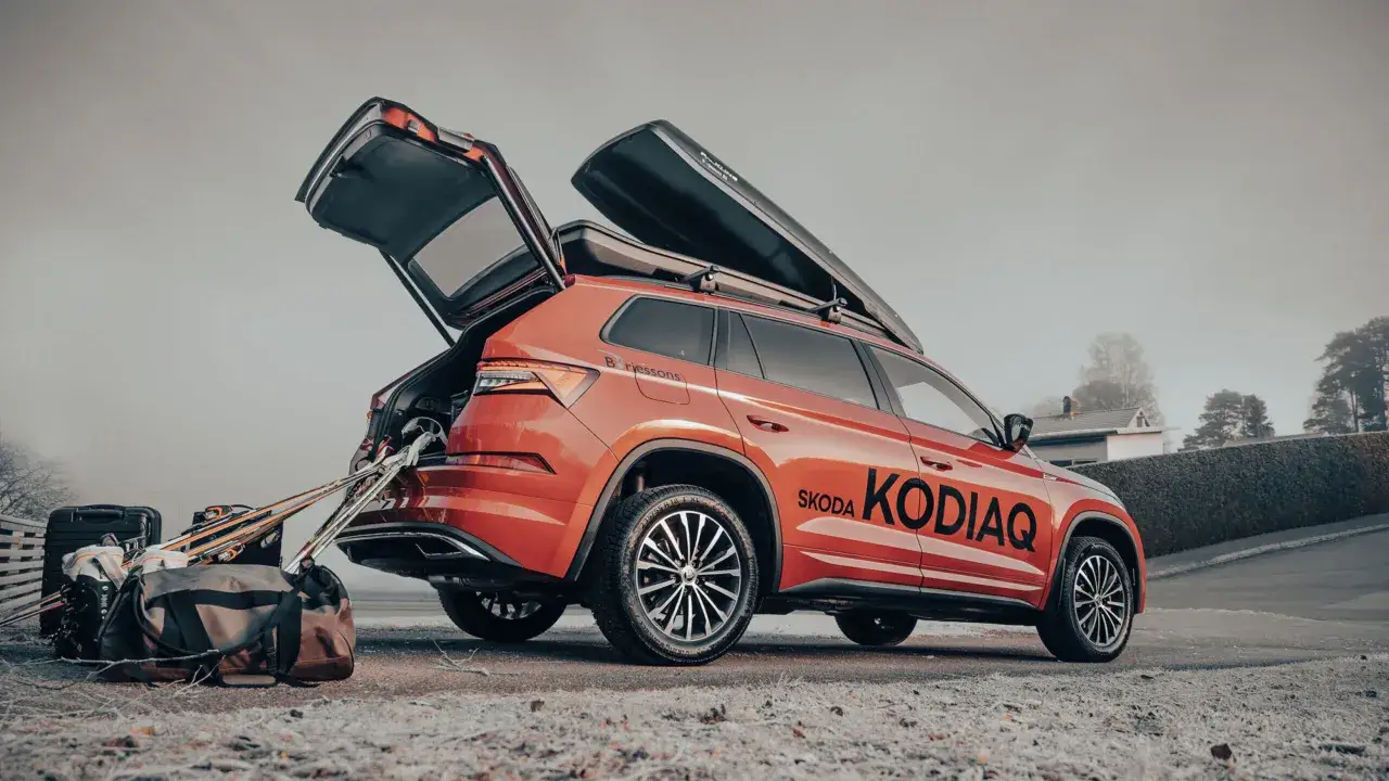 R&ouml;d Skoda Kodiaq redo f&ouml;r vinterns &auml;ventyr med takboxar och packning. Skidutrustning och v&auml;skor st&aring;r redo vid den &ouml;ppna bakluckan.