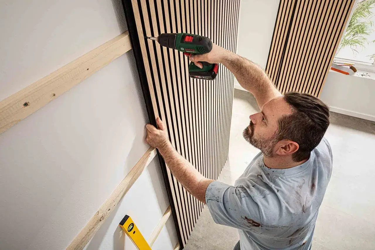Man monterar diy akustikpanel med skruvdragare. Tr&auml;ribbor p&aring; v&auml;ggen ger ett modernt utseende.
