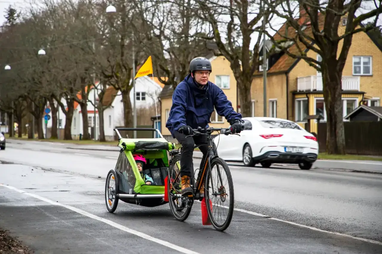 Man cyklar med barn i en Thule Coaster XT-vagn på en gata i Sverige.