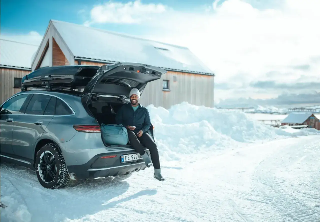 Man med en Thule skidbox p&aring; taket sitter vid bakluckan p&aring; en bil i sn&ouml;.
