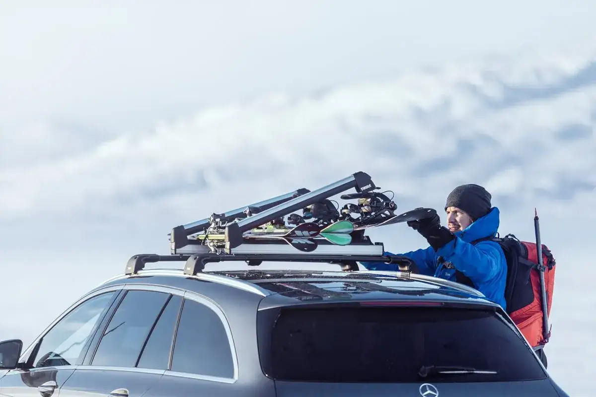 Man lastar skidor p&aring; en takbox smal. Sn&ouml;kl&auml;dda berg i bakgrunden.