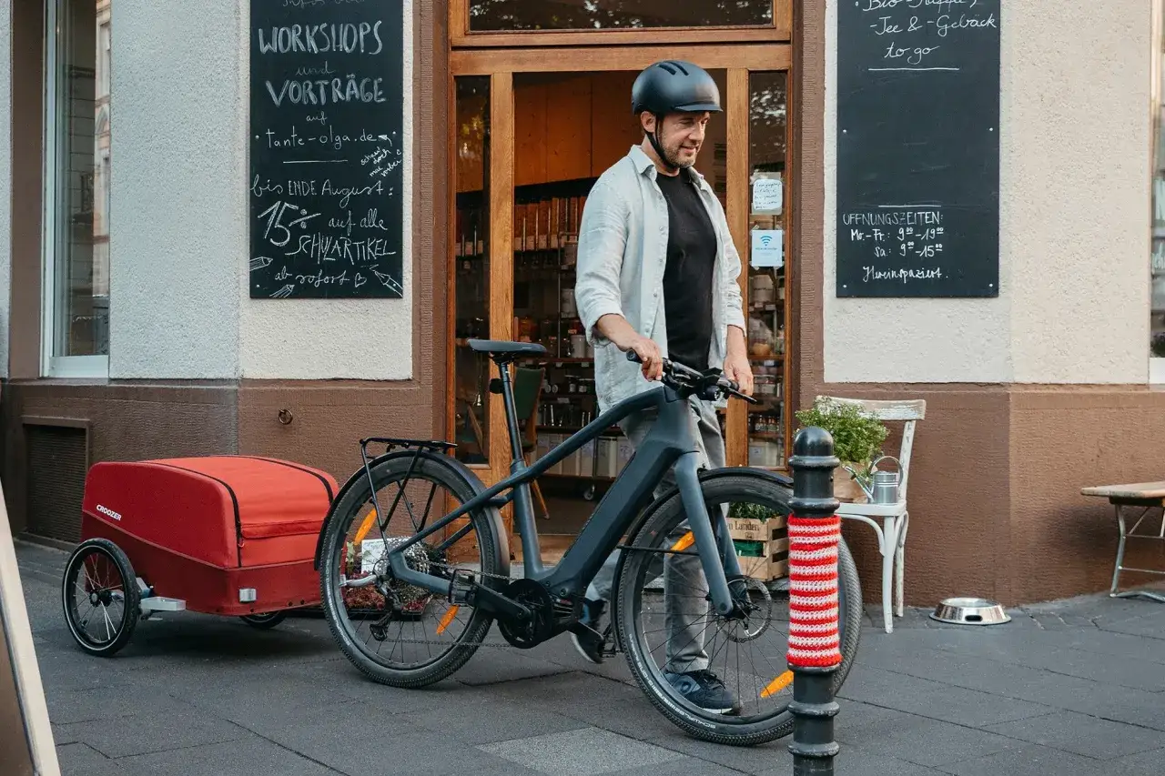 Man med cykel och en r&ouml;d spectra cykelvagn parkerad utanf&ouml;r en butik.