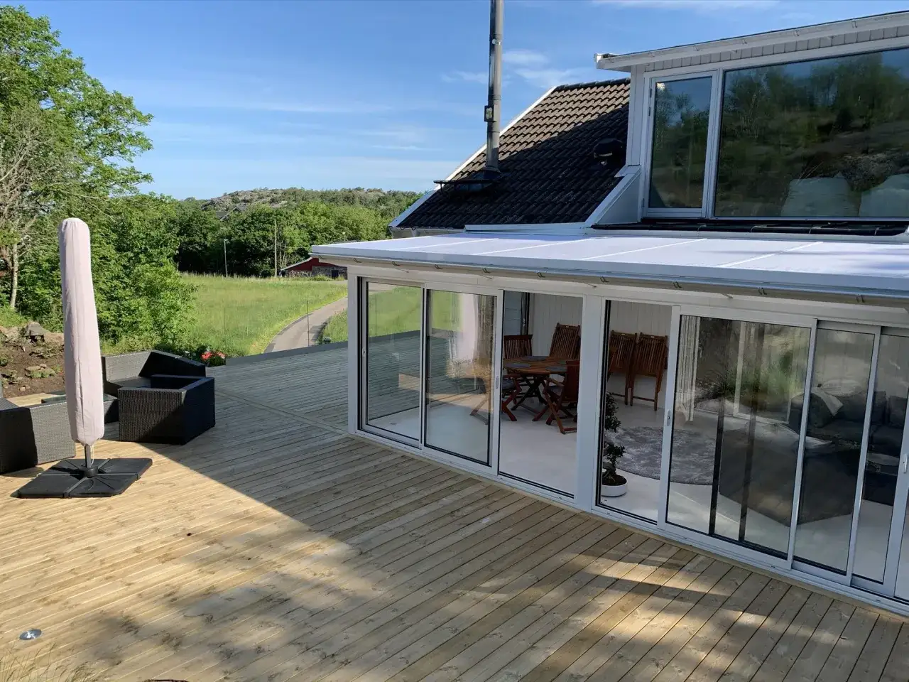 Nyligen slipad altan i trä med glasveranda och utemöbler. Solen lyser på den fina träytan.