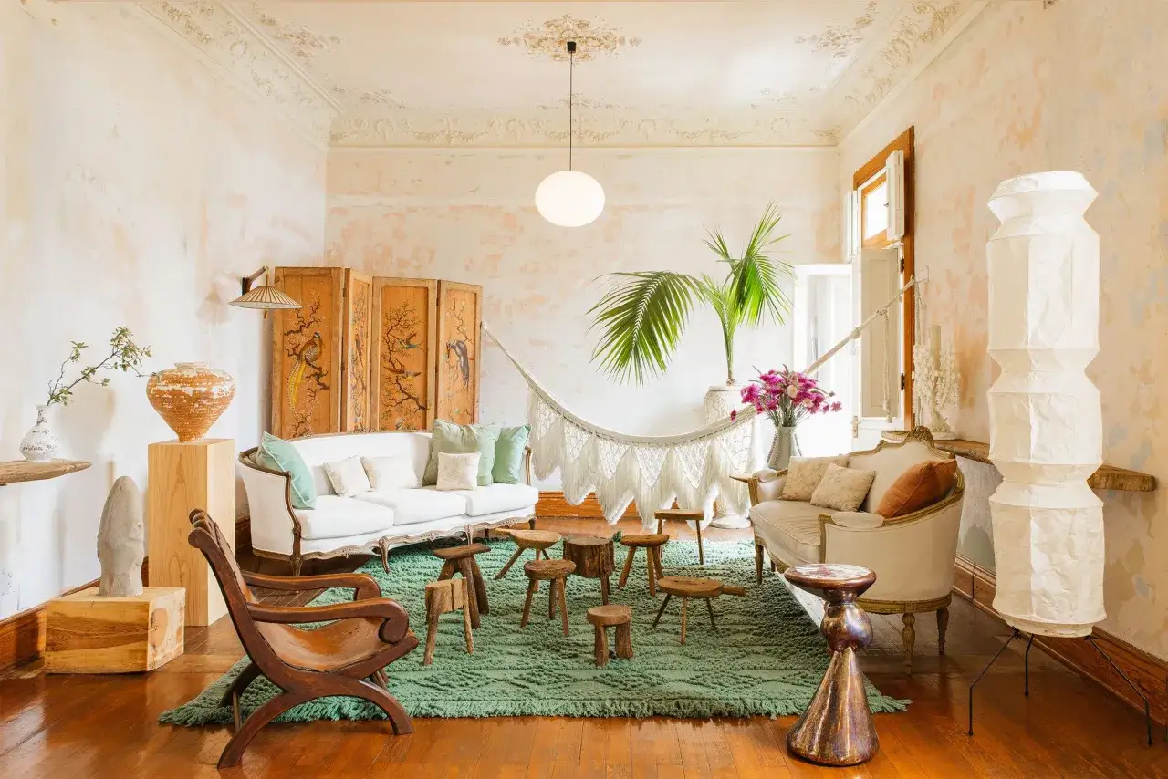 En avslappnad salong med boho chic inredning: vit soffa, makraméhängmatta, trästolar, grönt jutematta och en palm.