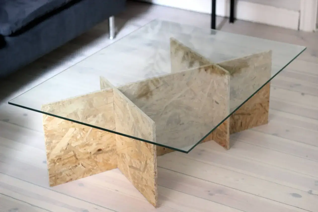 Ett unikt diy soffbord med glasskiva och en bas av OSB-skivor, skapad med en innovativ korsad design.