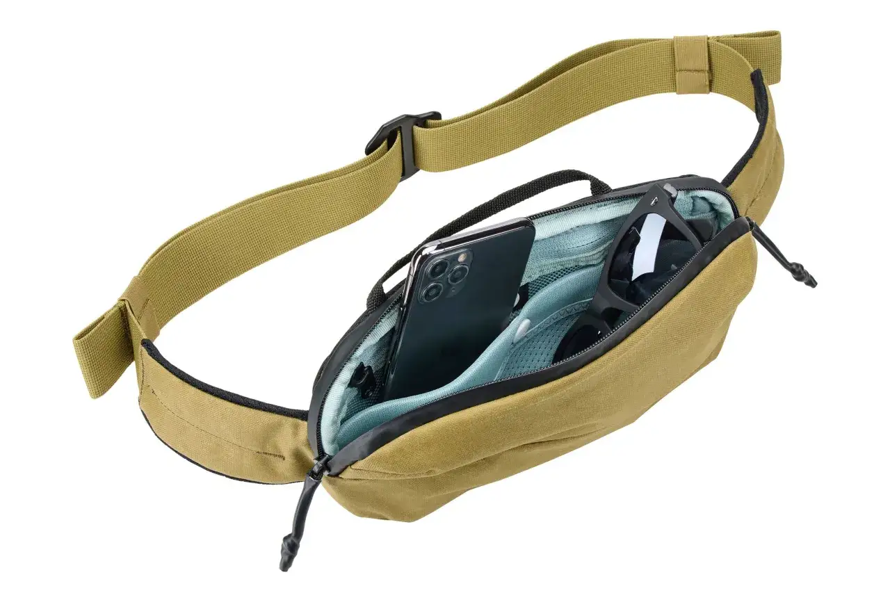 En Thule sling i kamouflagef&auml;rg med en mobiltelefon och solglas&ouml;gon i facket. Perfekt f&ouml;r &auml;ventyr.