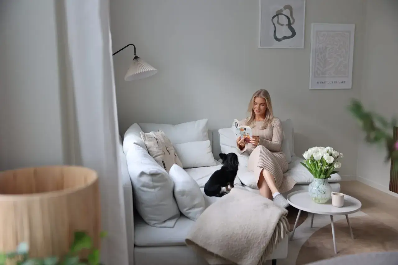 En kvinna l&auml;ser en bok i en mysig soffa med sin hund. En fin inspiration f&ouml;r att m&aring;la vardagsrummet i lugna f&auml;rger.