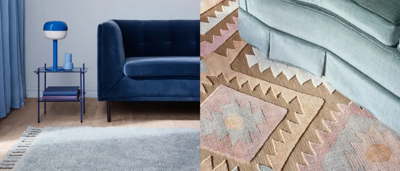 En mjuk, ljusblå matta med fransar ligger framför en mörkblå sammetssoffa. Bredvid syns en mönstrad matta med geometriska former i rosa, beige och grått, som matchar en ljusblå soffa.