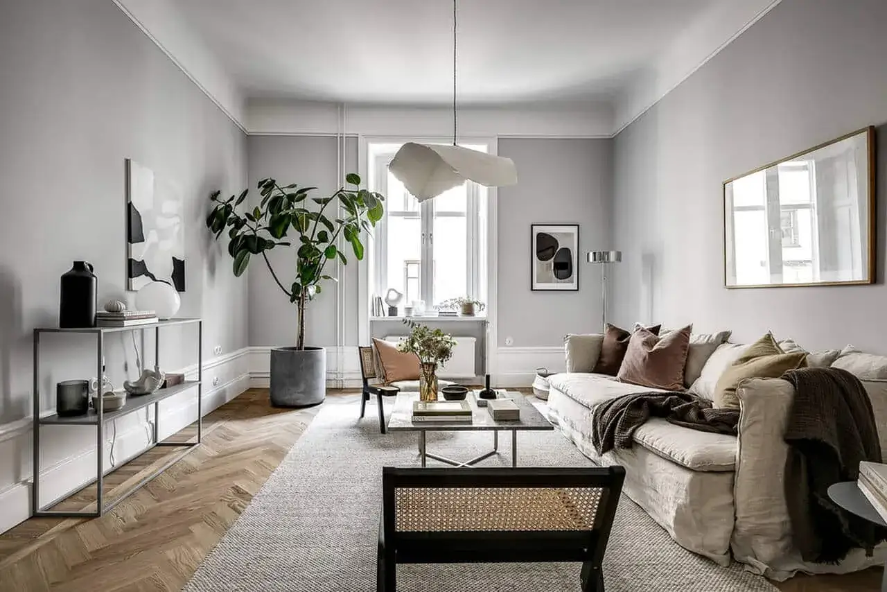 Ett stilrent gr&aring;tt och beige vardagsrum med en stor soffa, kaffebord, en gr&ouml;n v&auml;xt och konst p&aring; v&auml;ggen.