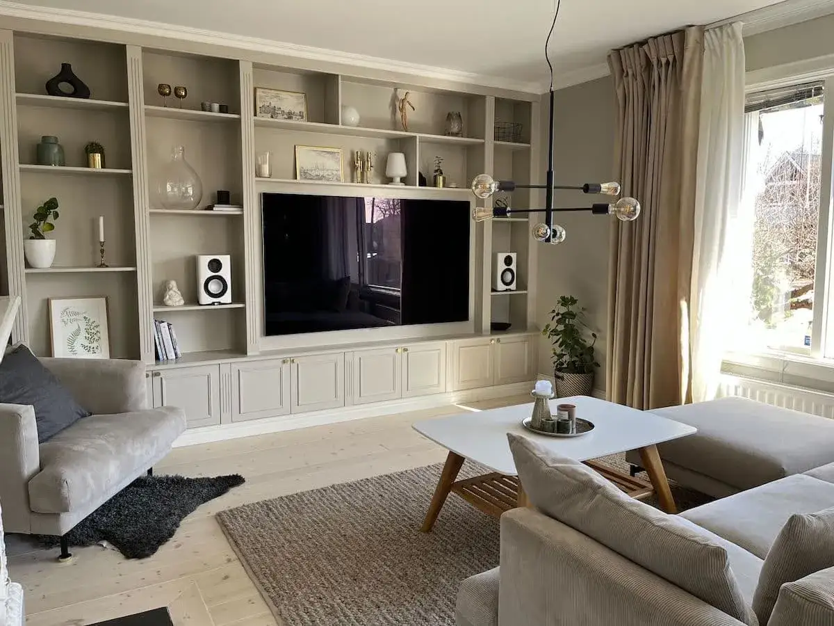 En elegant platsbyggd bokhylla med integrerad TV och f&ouml;rvaring. Hyllorna &auml;r dekorerade med konst, v&auml;xter och h&ouml;gtalare.