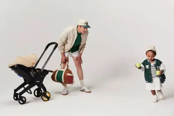 En man med en barnvagn och en sportväska. Barnet leker med tennisbollar. Bältesskydd barnvagn för extra komfort.