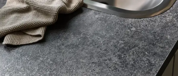 En mörk, stenig laminatskiva med en beige kökshandduk vid diskho.