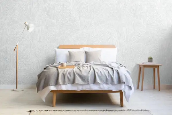 Sovrum med säng, grå pläd, träbricka med mugg och en golvlampa. Vacker tapet med organiskt mönster skapar en lugn boho chic inredning.