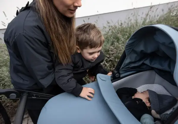 En mamma och ett barn tittar ner på en sovande bebis i en Thule Urban Glide liggdel.