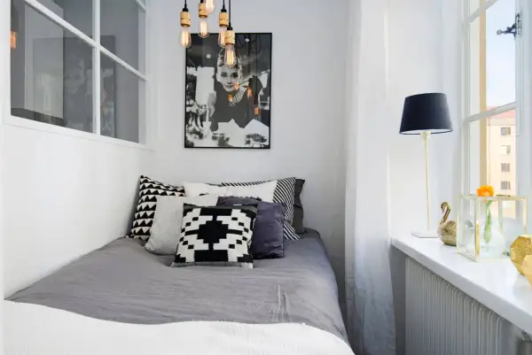 Stilren inredning litet sovrum med Audrey Hepburn-poster, grå sängkläder och grafiska kuddar. En golvlampa och en blomma på fönsterbrädan.
