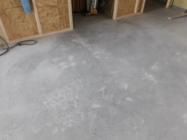 Ett rått betonggolv som väntar på att slipas. Verktyg och byggmaterial syns i bakgrunden.