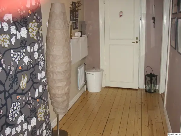En inreda långsmal hall med en stor golvlampa, en vit dörr och en svart lykta.