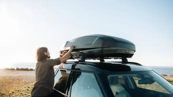 Man justerar en Thule lastbox på taket av en bil vid havet.